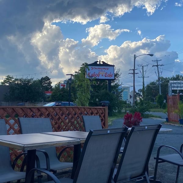 Outdoor patio seating with tables and chairs, a Yummy Kabob Cafe sign, and cloudy blue sky.