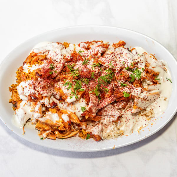 Chicken and rice platter topped with creamy white sauce, red spice, and fresh green herbs.