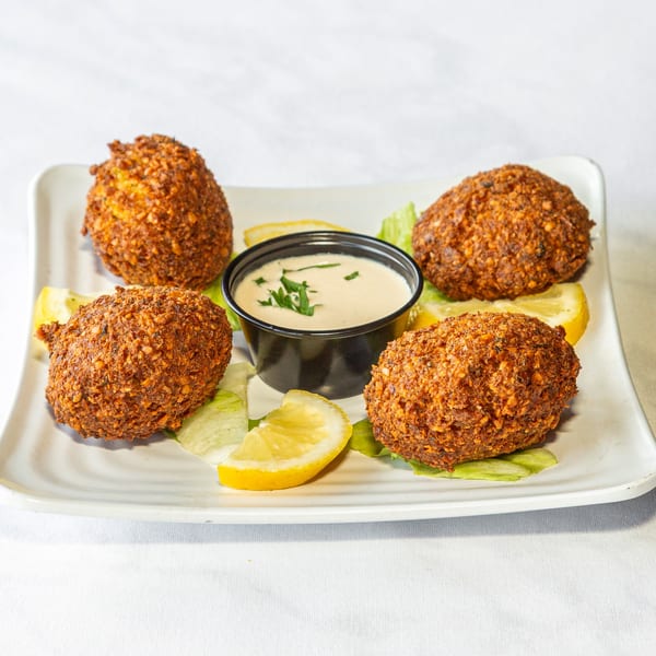 Four crispy falafel balls with tahini sauce, lemon wedges, and lettuce on a white plate.