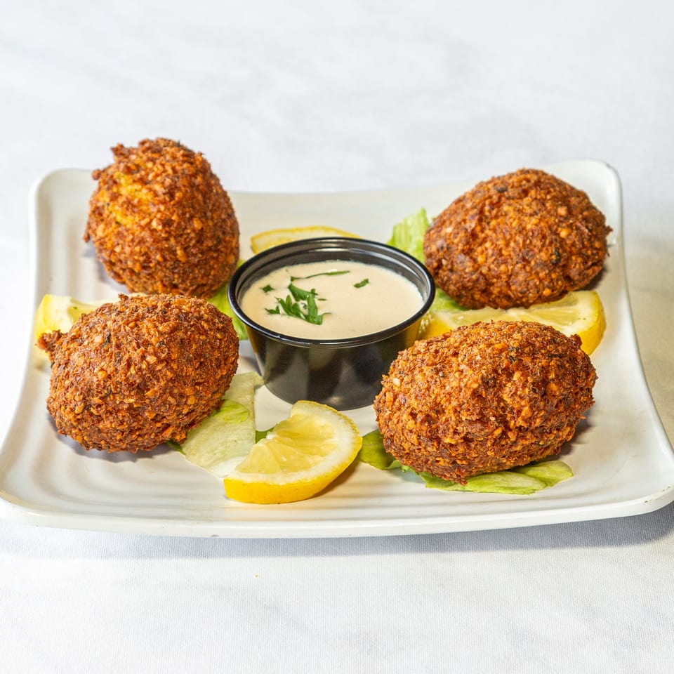 Four crispy falafel balls with tahini sauce, lemon wedges, and lettuce on a white plate.