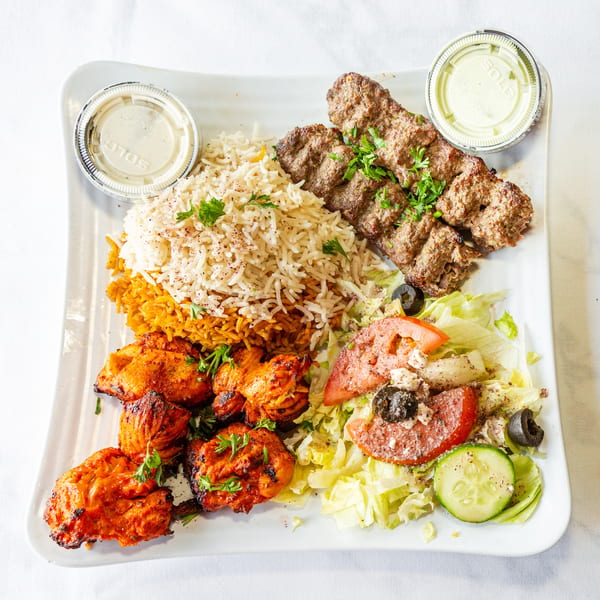 Grilled chicken and beef kebabs with rice, salad, and sauces on a white plate.