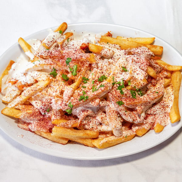 French fries covered in creamy white sauce, red spice, and fresh parsley on a white plate.