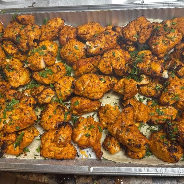 Tray of grilled, spice-marinated chicken pieces garnished with cilantro over flatbread.