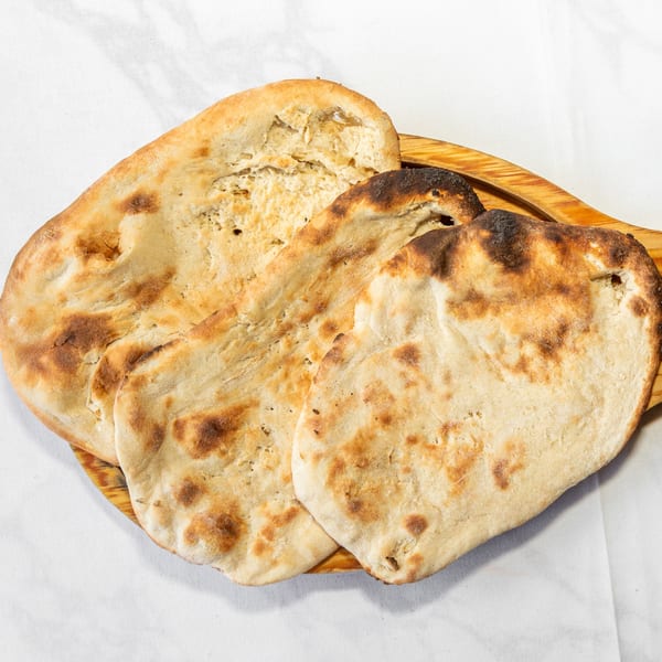Three pieces of golden-brown flatbread with charred spots on a wooden board.