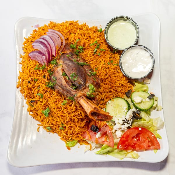 Lamb shank with seasoned rice, red onions, side salad, and two sauces on a white plate.