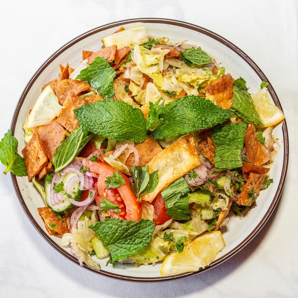 Delicious Fattoush salad with fresh vegetables, crispy pita, mint, and lemon on a white tablecloth.