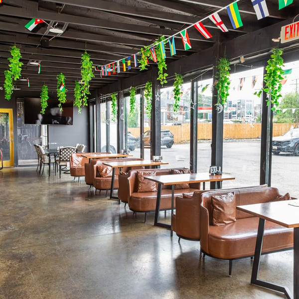 Modern restaurant interior with brown leather booths, concrete floor, large windows, and international flag decor.