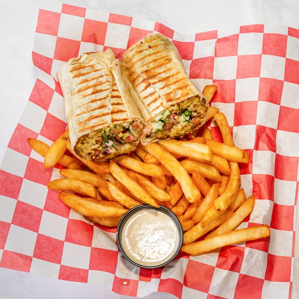 Two grilled wraps filled with falafel and vegetables, served with seasoned fries and dipping sauce.